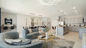 Un soggiorno moderno con un divano grigio, un tavolino rotondo e un'area pranzo illuminata da un lampadario.