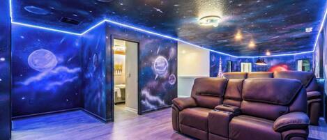 A room with a space-themed ceiling, a leather sofa, and a door leading to another room.