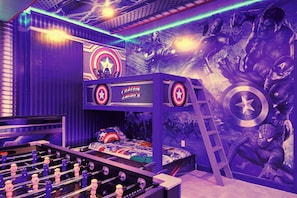 A room with a bunk bed, a foosball table, and a wall mural featuring superhero characters.