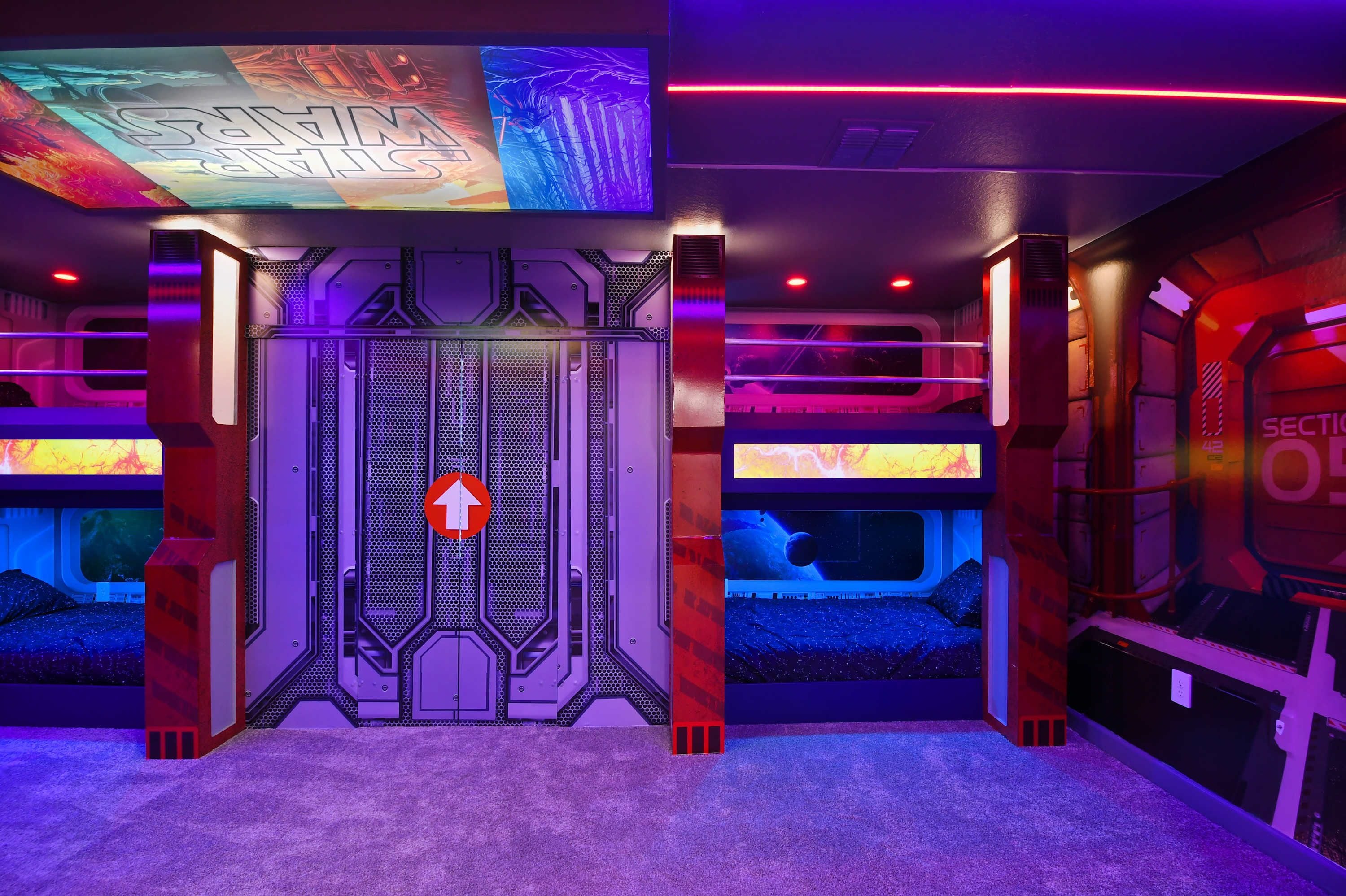 A room with a futuristic design, featuring a central door with a directional arrow sign, surrounded by walls with hexagonal patterns and ambient lighting.