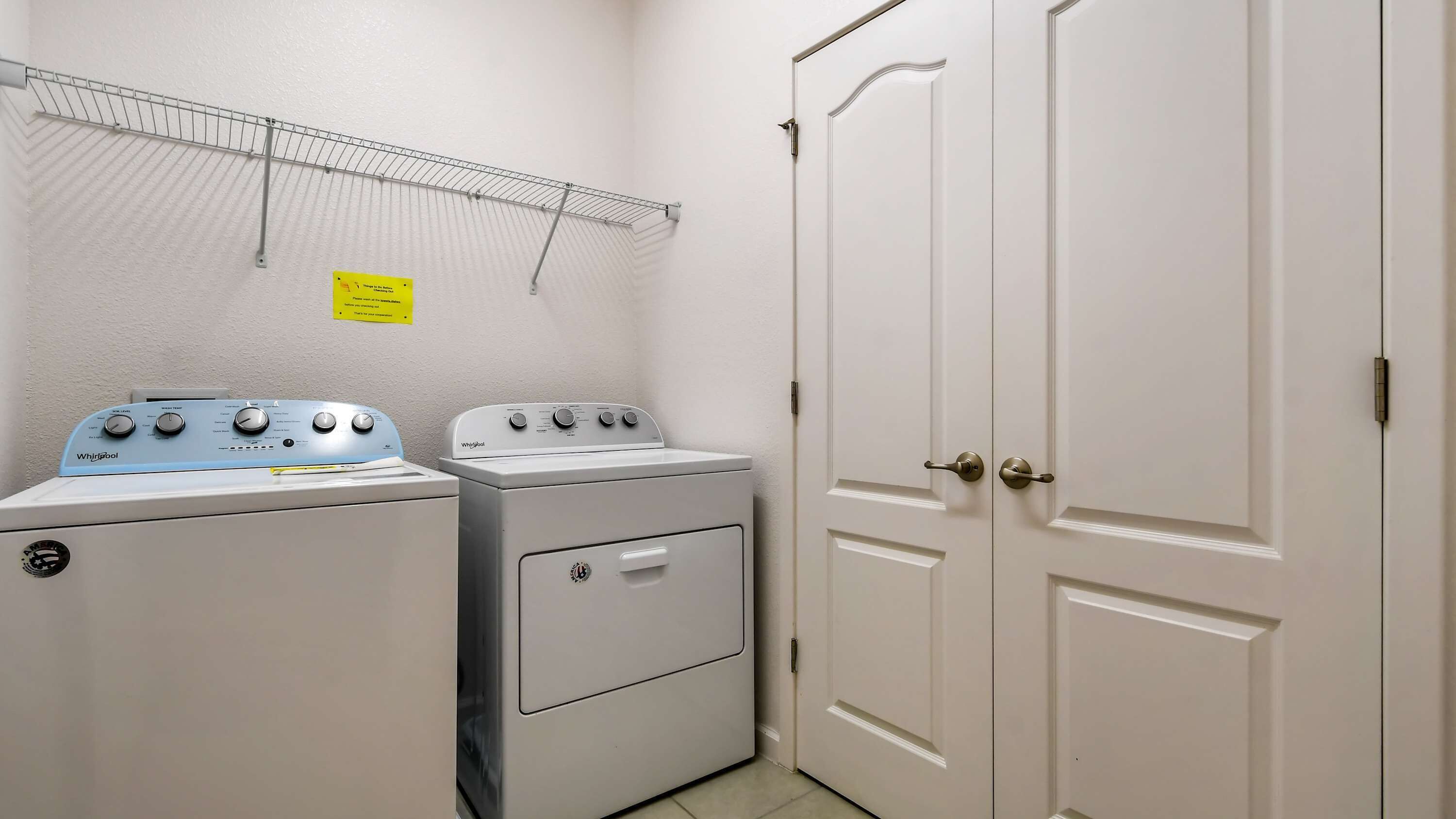A laundry room with two Whirlpool washers and dryers, a metal drying rack, and a door with a handle.