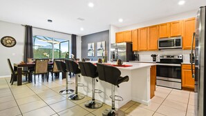 A modern kitchen with wooden cabinets, stainless steel appliances, and a dining area with bar stools. - Veranda Plams 9BR Villa Private Pool Spa 2570 (Kissimmee)