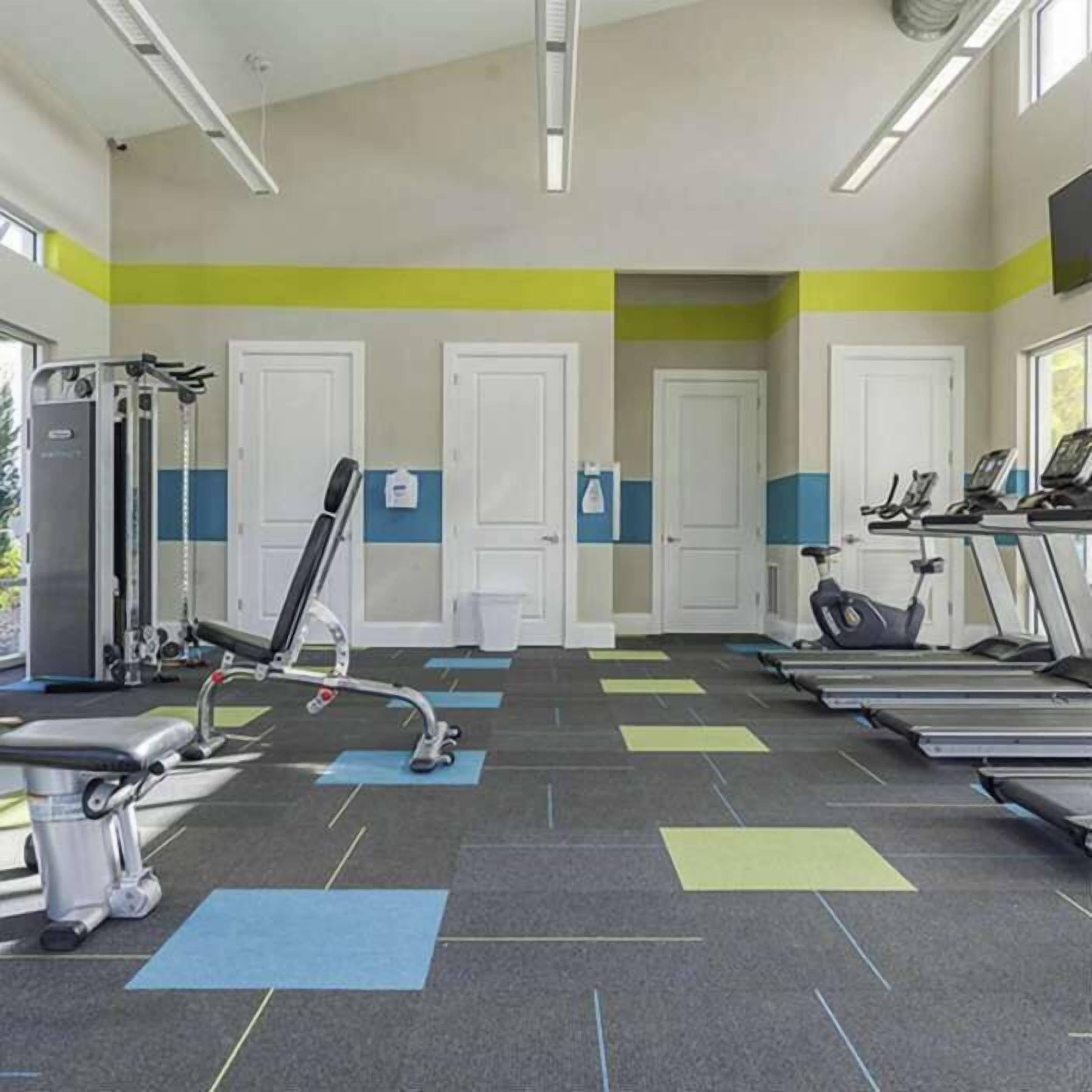 Un gimnasio con equipo de ejercicio, cintas de correr y una televisión instalada en la pared.