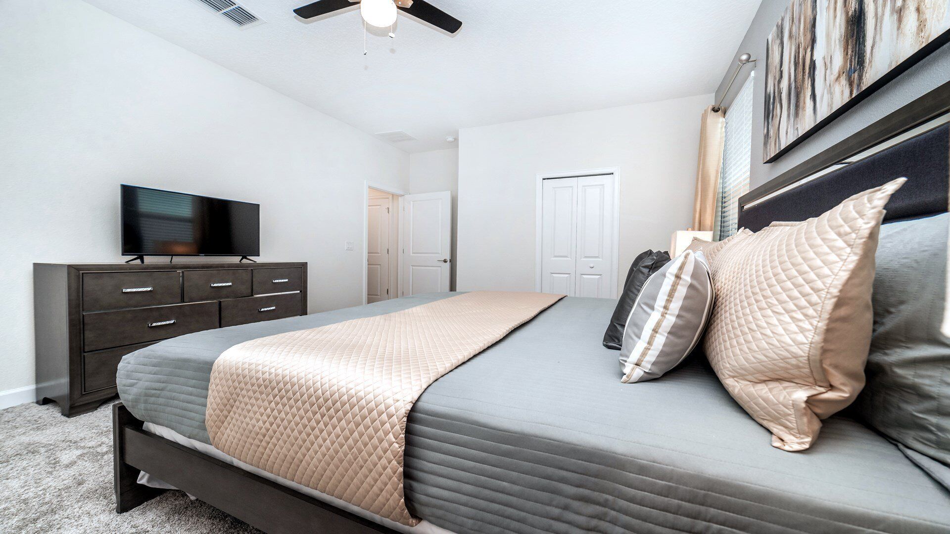 Une chambre à coucher avec un lit, un téléviseur posé sur une commode et un ventilateur de plafond.