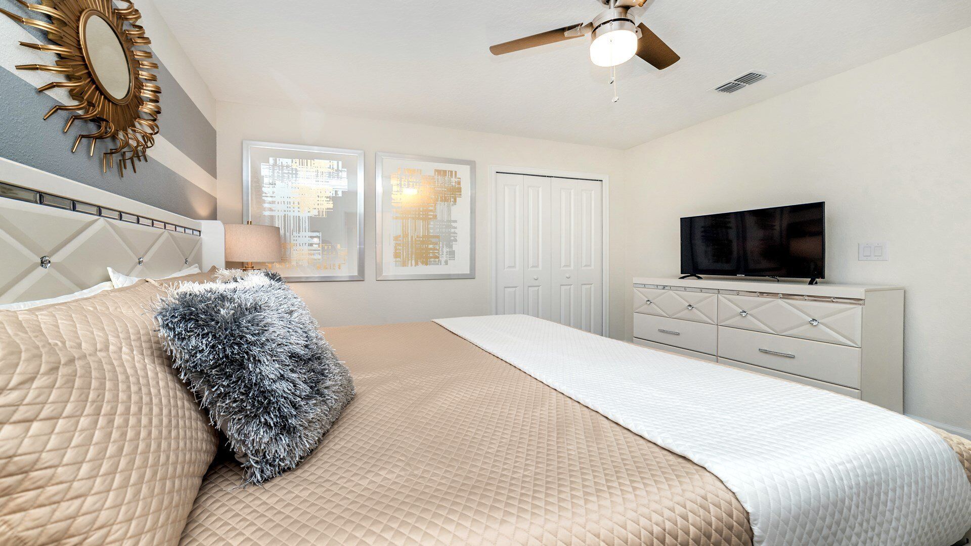 A bedroom with a bed, a ceiling fan, a TV, and a dresser.