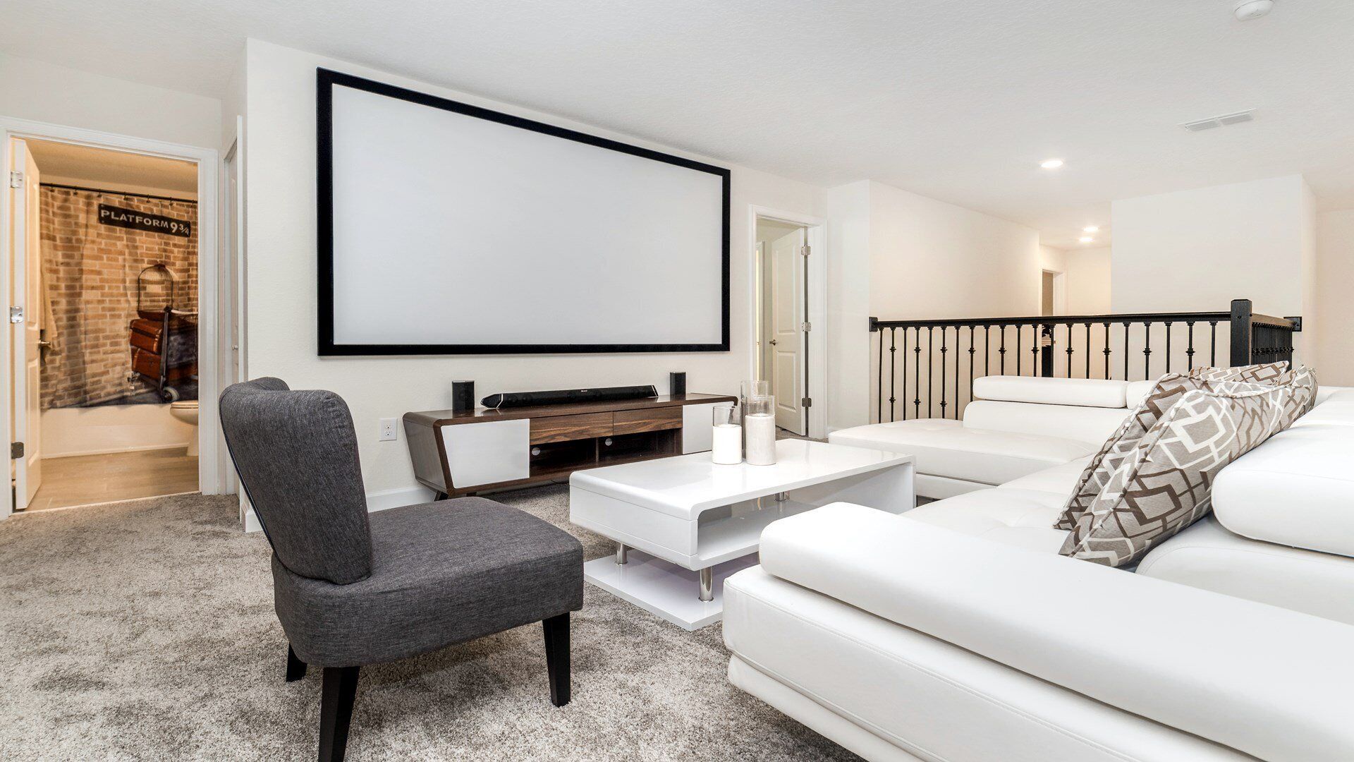 A modern living room with a white sofa, a grey armchair, a coffee table, and a large TV screen.