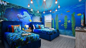 Une chambre avec deux lits, une table de chevet et une commode. La pièce est décorée d’une fresque représentant un paysage sous-marin avec des poissons et des coraux.