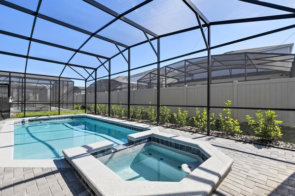 Une piscine avec un jacuzzi, le tout entouré d’une structure en verre et doté d’une armature métallique.