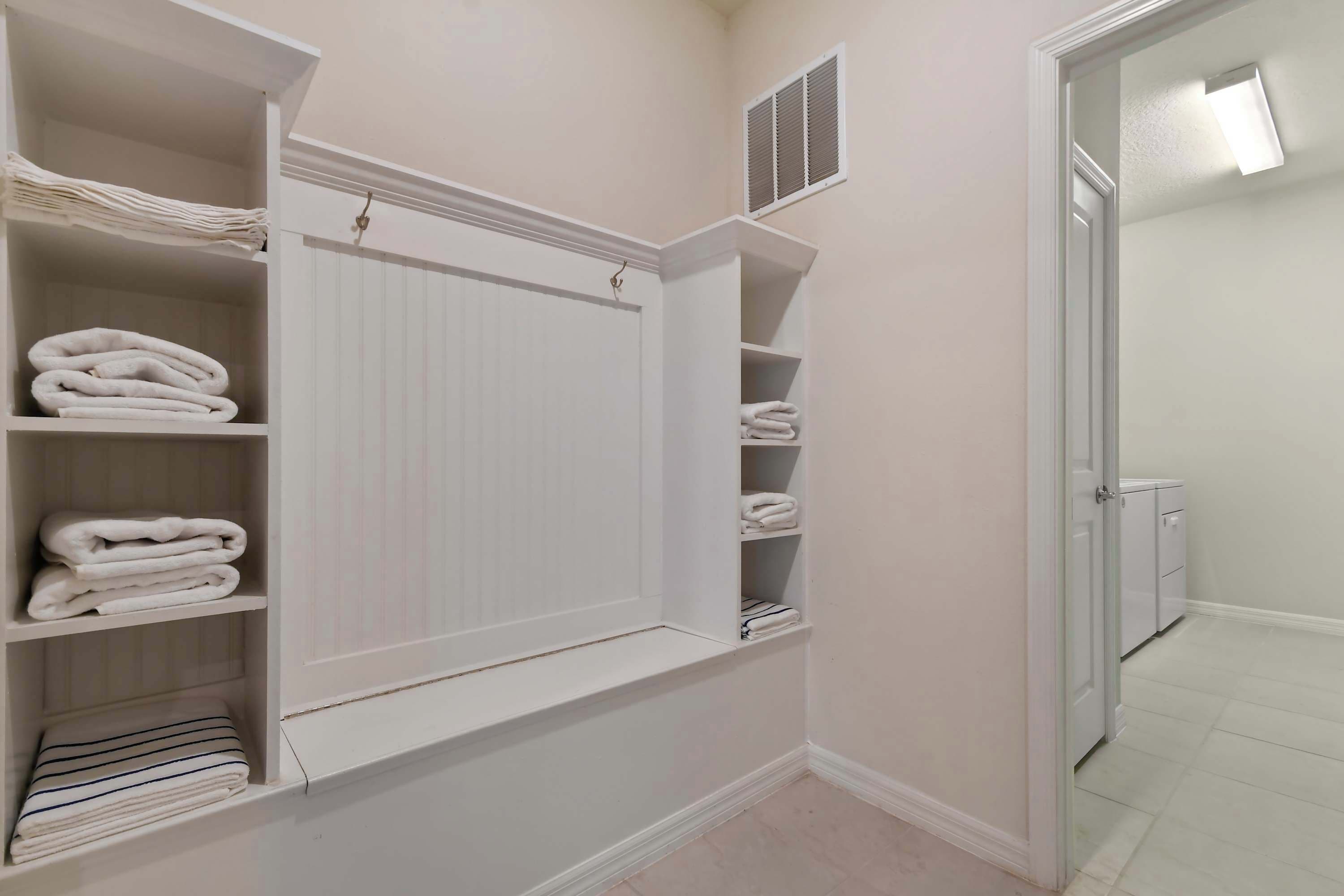A bathroom with a white radiator, shelves with folded towels, and a white door leading to another room.