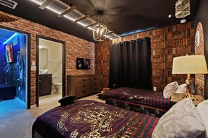 Een kamer met een bakstenen muur, een boekenplank, een bed met beddengoed met een patroon, een bureau met een lamp en een televisie aan de muur.