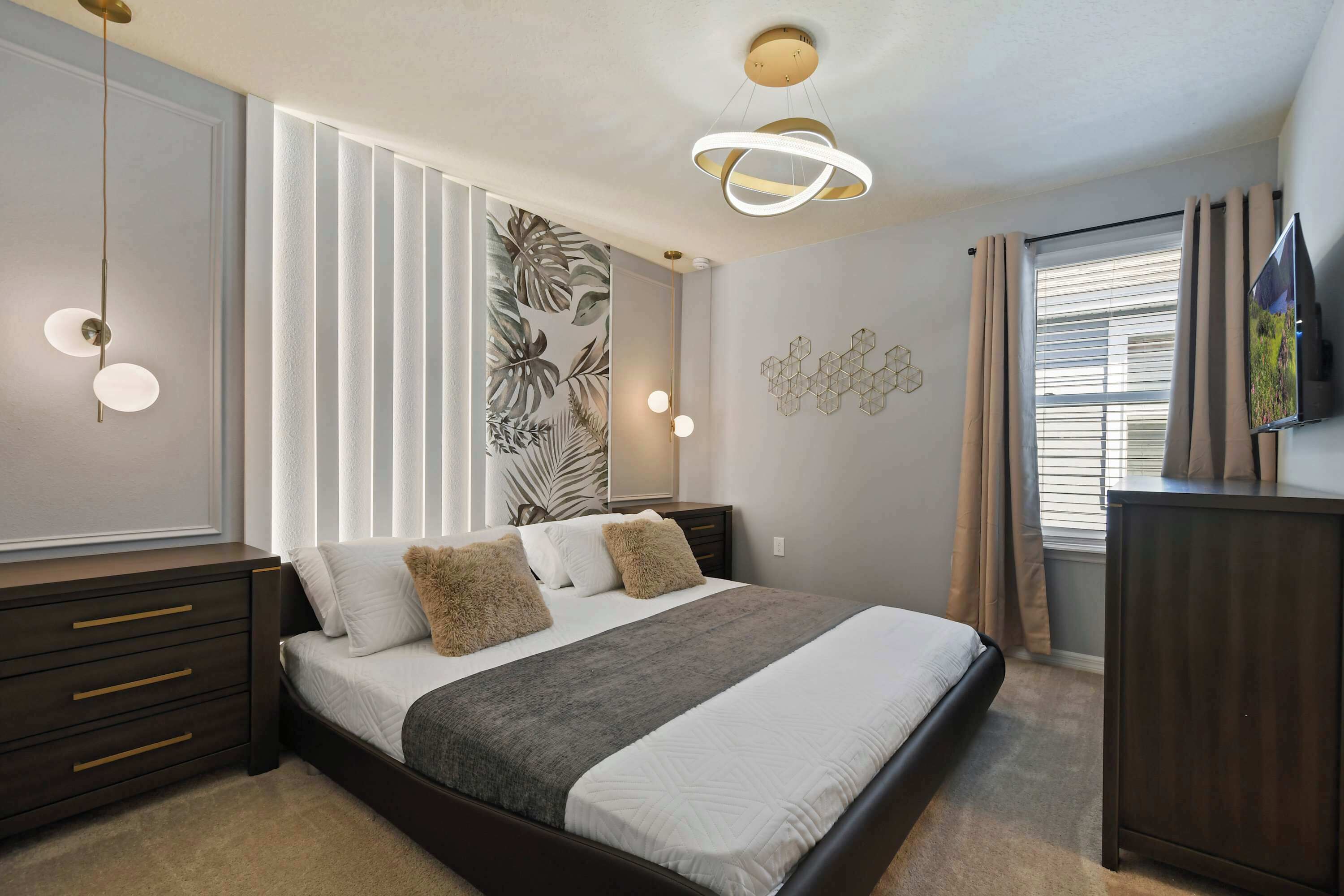 A modern bedroom with a large bed, bedside tables, a wall-mounted TV, and a ceiling light fixture.
