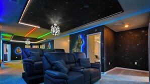 A room with a black leather sofa, a ceiling with star projections, and a wall with a space-themed mural. - Fancy Game Theater 10br Villa W/pool/spa Disney (Davenport)