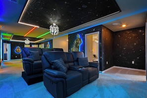 Une pièce avec un canapé en cuir noir, un plafond orné de projections d’étoiles et un mur décoré d’une fresque sur le thème de l’espace.