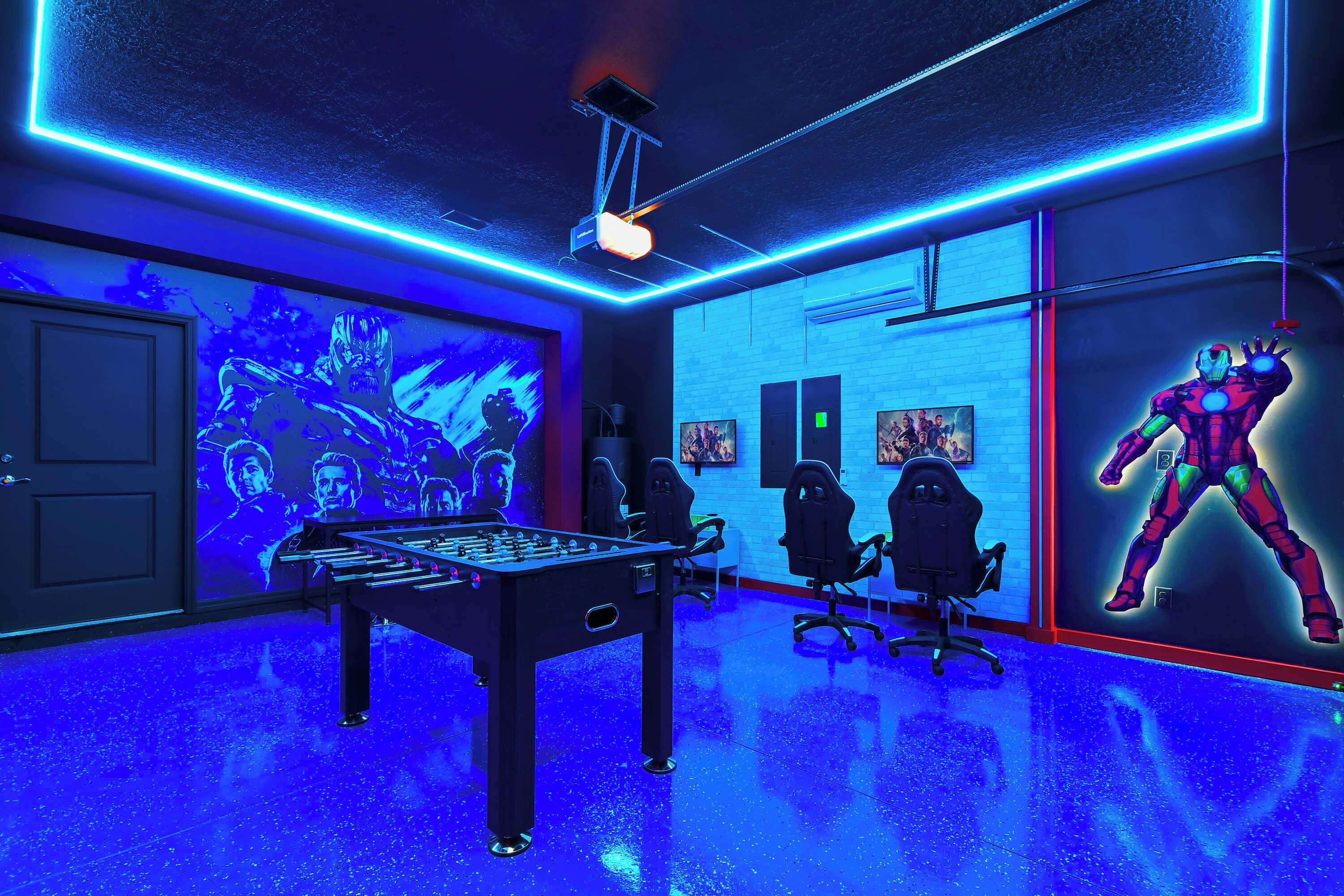 A room with a foosball table, gaming chairs, and a large screen displaying a movie.