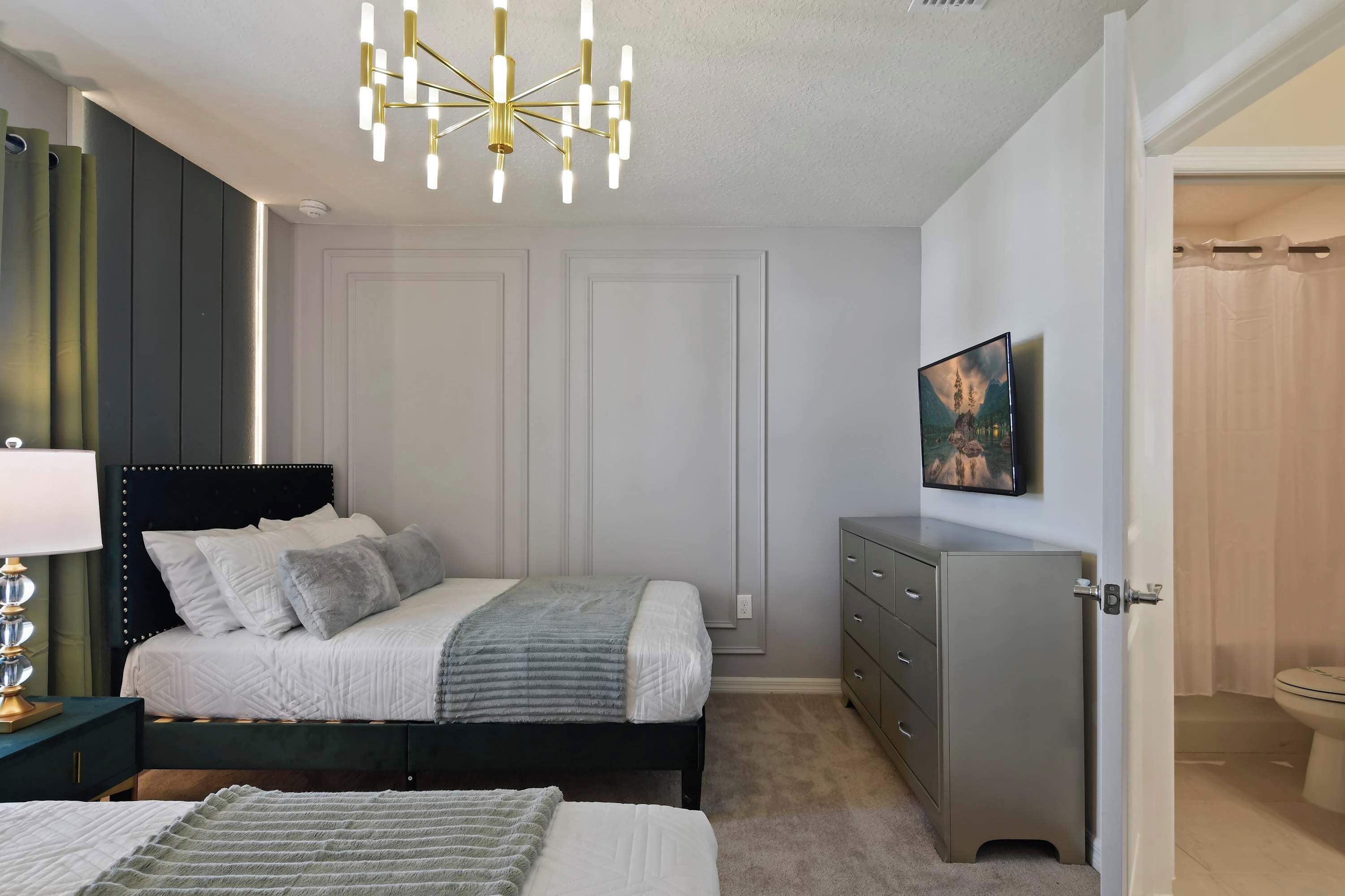 A bedroom with a bed, bedside tables, a dresser, a painting, and a chandelier.