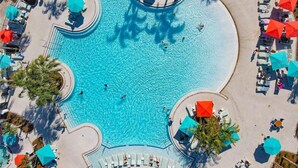 An aerial view of a resort with a large central swimming pool surrounded by sun loungers and umbrellas. - Fancy Game Theater 10br Villa W/pool/spa Disney (Davenport)