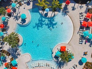 Vue aérienne d’un complexe hôtelier doté d’une grande piscine centrale, entourée de transats et de parasols.