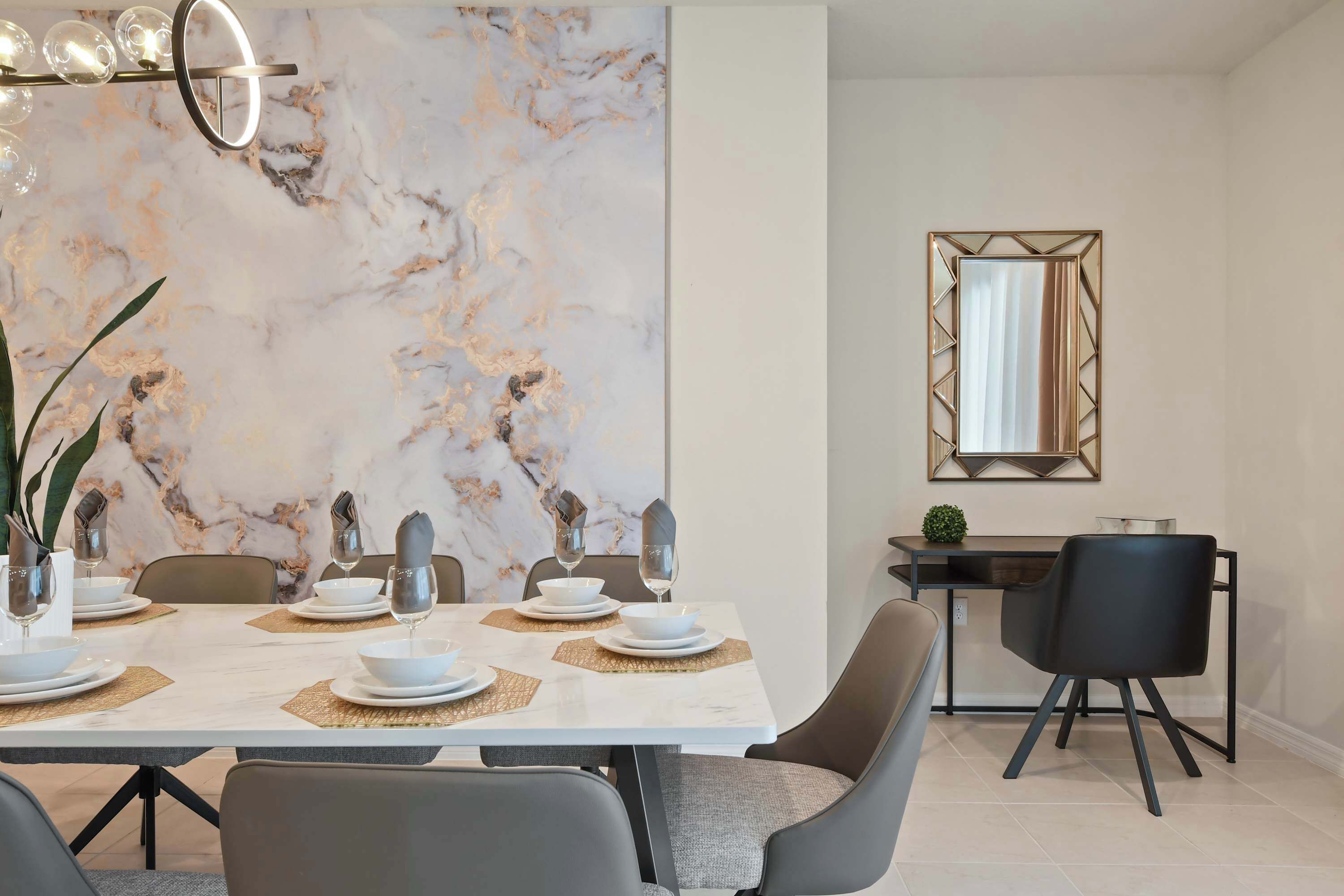 Un comedor moderno con una pared de mármol, una mesa de comedor dispuesta con platos, vasos y cubiertos, y un espejo en la pared.