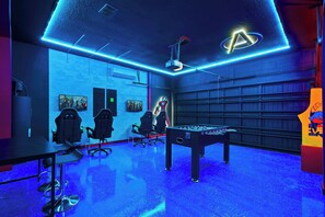 Une pièce équipée d’un baby-foot, de fauteuils de jeu et d’un écran de projection.