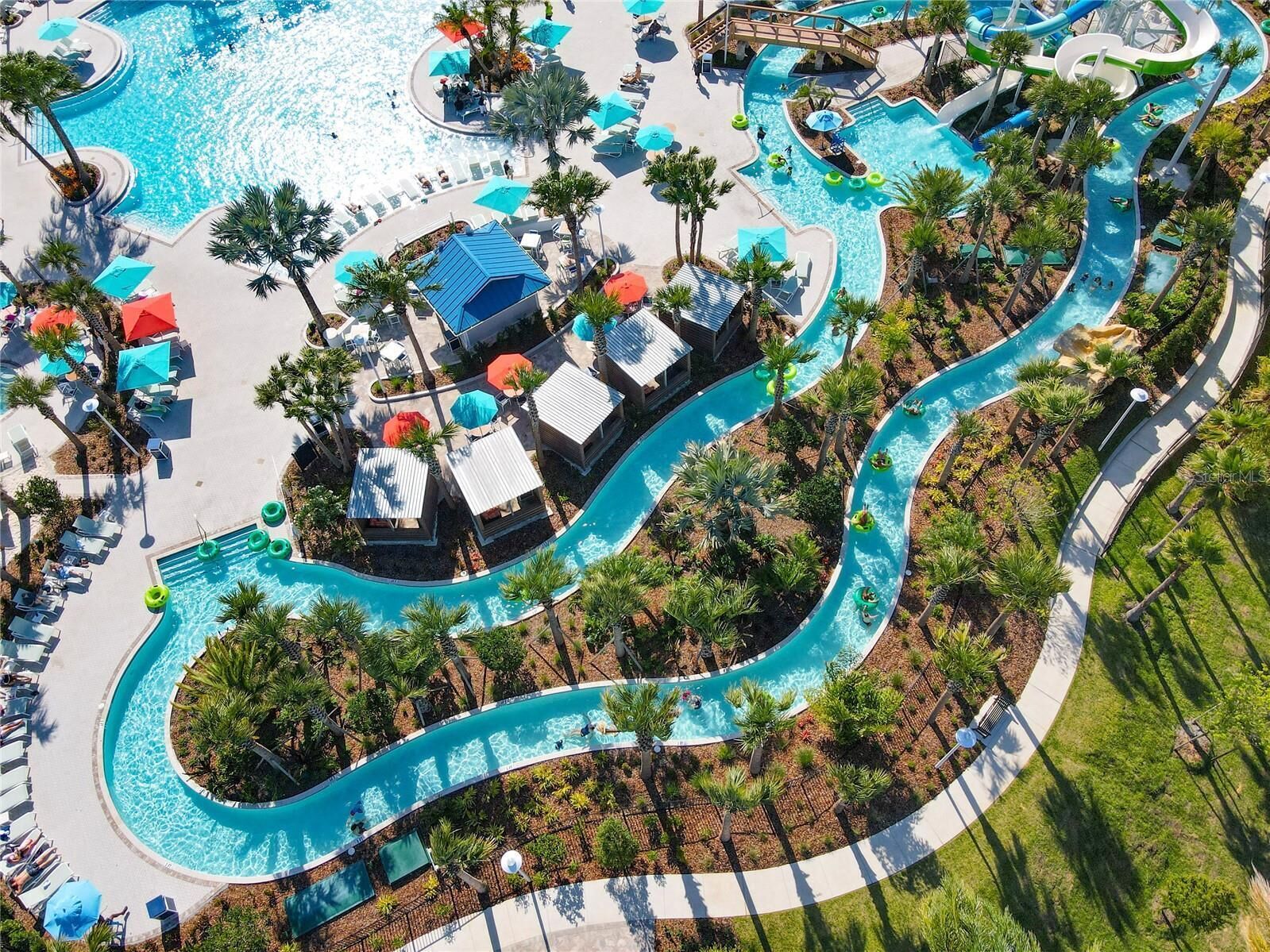 An aerial view of a resort with a winding pool, lounge areas, and palm trees.