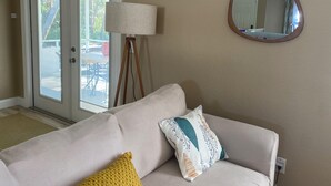 Uma sala de estar com um sofá bege, uma almofada estampada, um abajur e um espelho na parede.