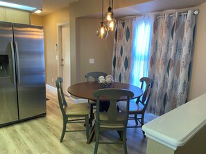A dining area with a round table, four chairs, a refrigerator, and a decorative light fixture. - FALL SPECIAL 15% off through December! FULLY FURNISHED,COZY COTTAGE (North Port)