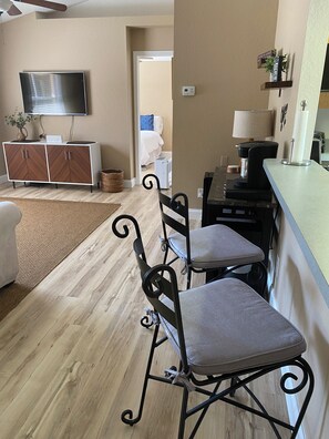 A modern kitchen with a dining area, a flat-screen TV mounted above the counter, and a coffee machine. - FALL SPECIAL 15% off through December!  FULLY FURNISHED,COZY COTTAGE (North Port)