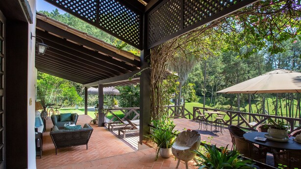 A covered patio with outdoor furniture, a table with an umbrella, and potted plants. - Sítio Dels Serrans - Jacareí (Jacarei)
