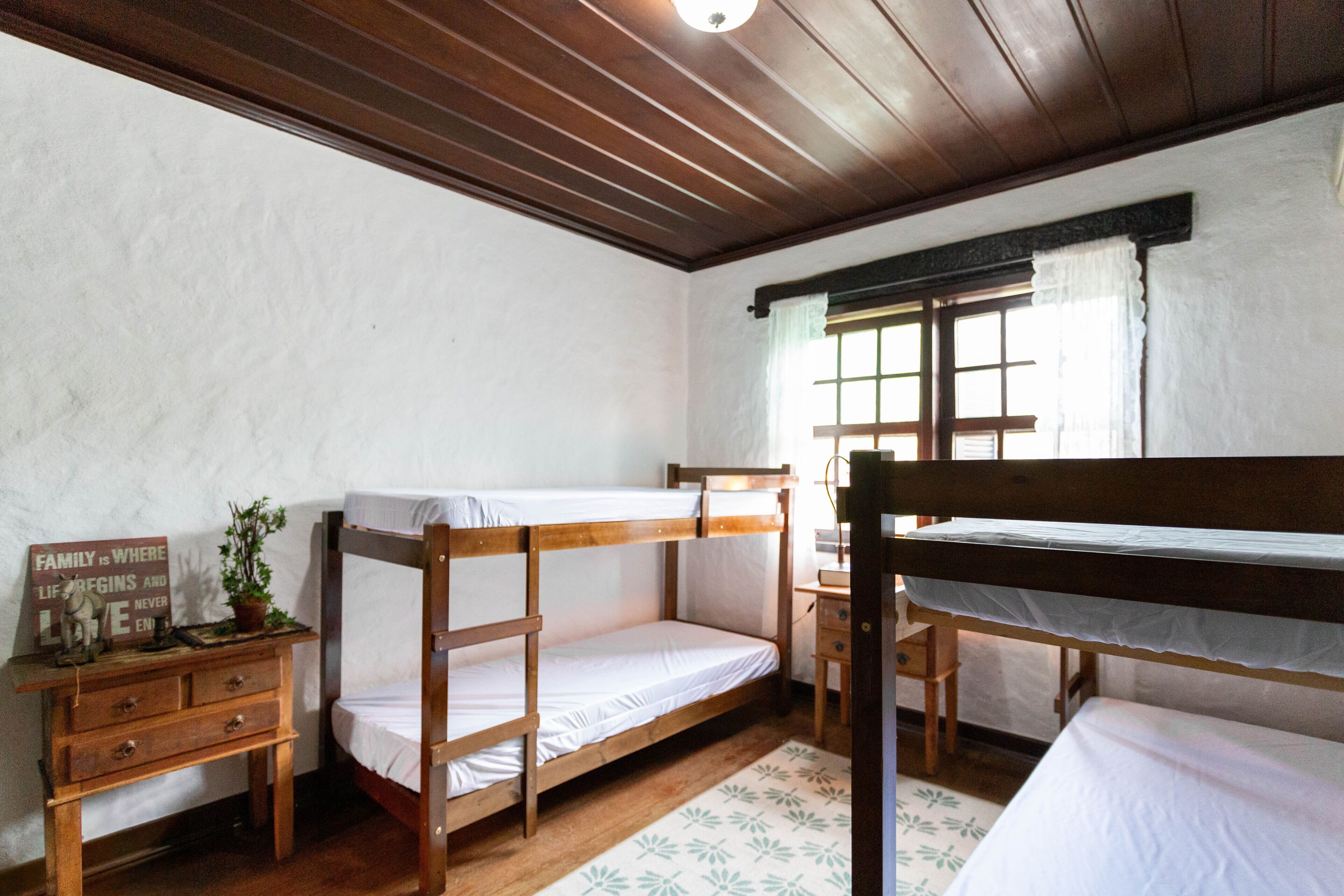 A room with two bunk beds, a wooden desk, a nightstand, and a window with curtains.