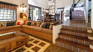 A spacious living area with a large sofa, wooden coffee table, and a fireplace. There is a staircase with colorful tiles leading to an upper level. - Sítio Dels Serrans - Jacareí (Jacarei)