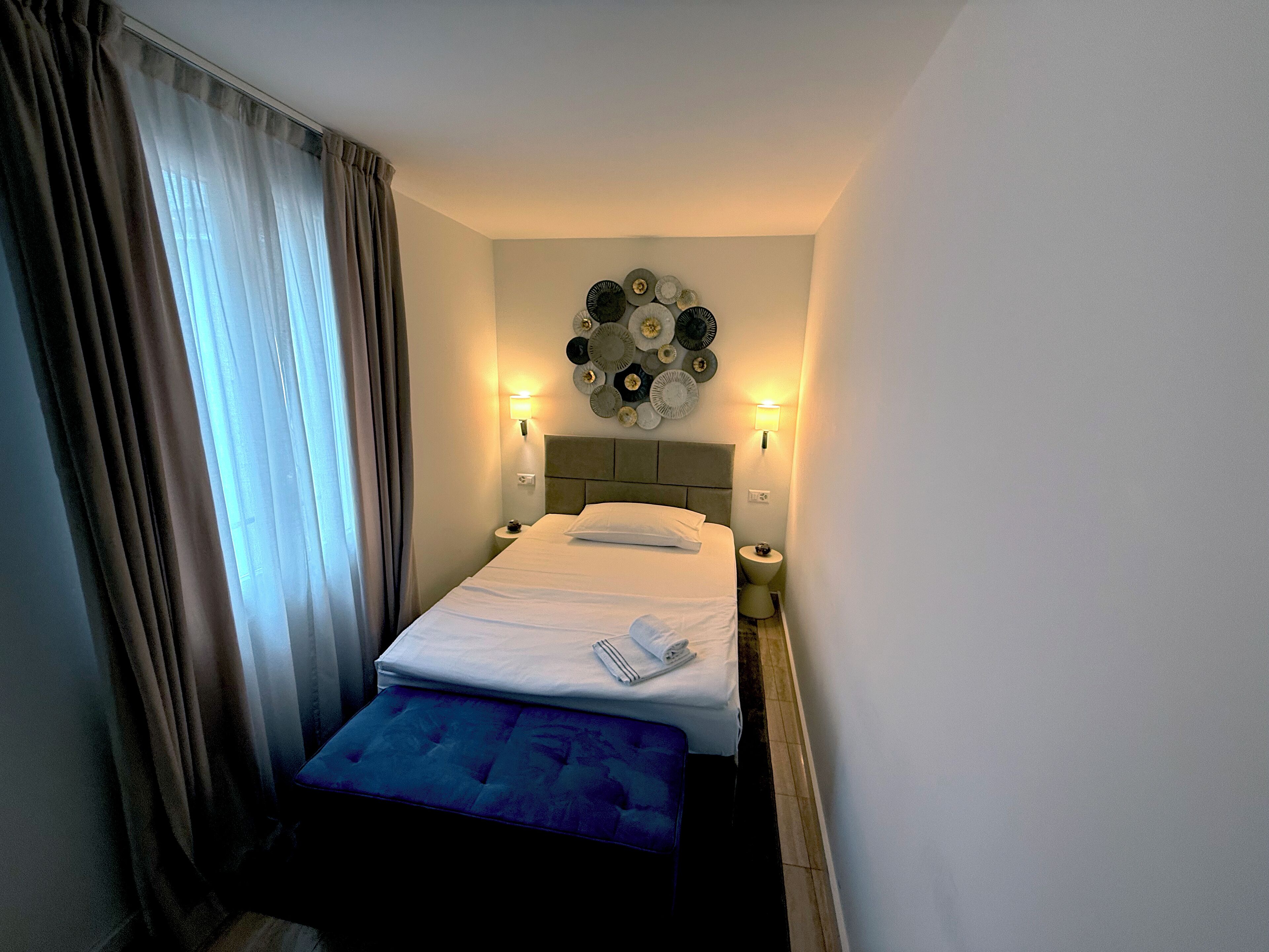 Una habitación de hotel con cama, lámparas de noche, un reloj de pared y una mesita.