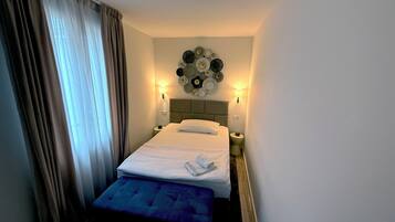 Una habitación de hotel con cama, lámparas de noche, un reloj de pared y una mesita.