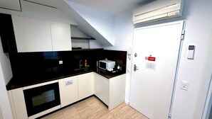 A modern kitchen with white cabinets, a black countertop, and an oven. There is a microwave, a sink, and a door with a sign. - San Carlo Apartments (Lugano)