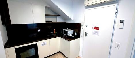 A modern kitchen with white cabinets, a black countertop, and an oven. There is a microwave, a sink, and a door with a sign.