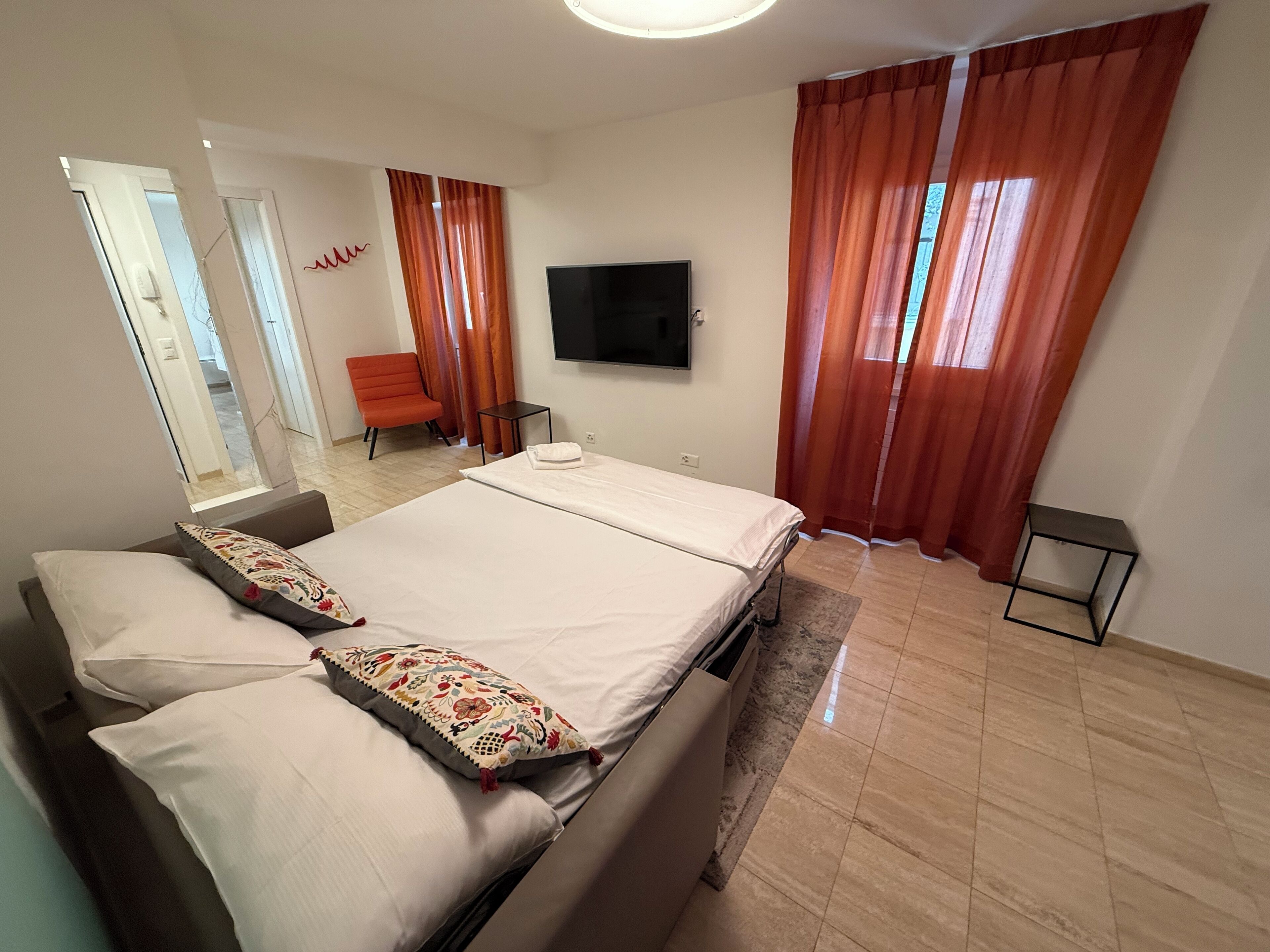 Una habitación de hotel con una cama, televisión, una silla y una mesita.