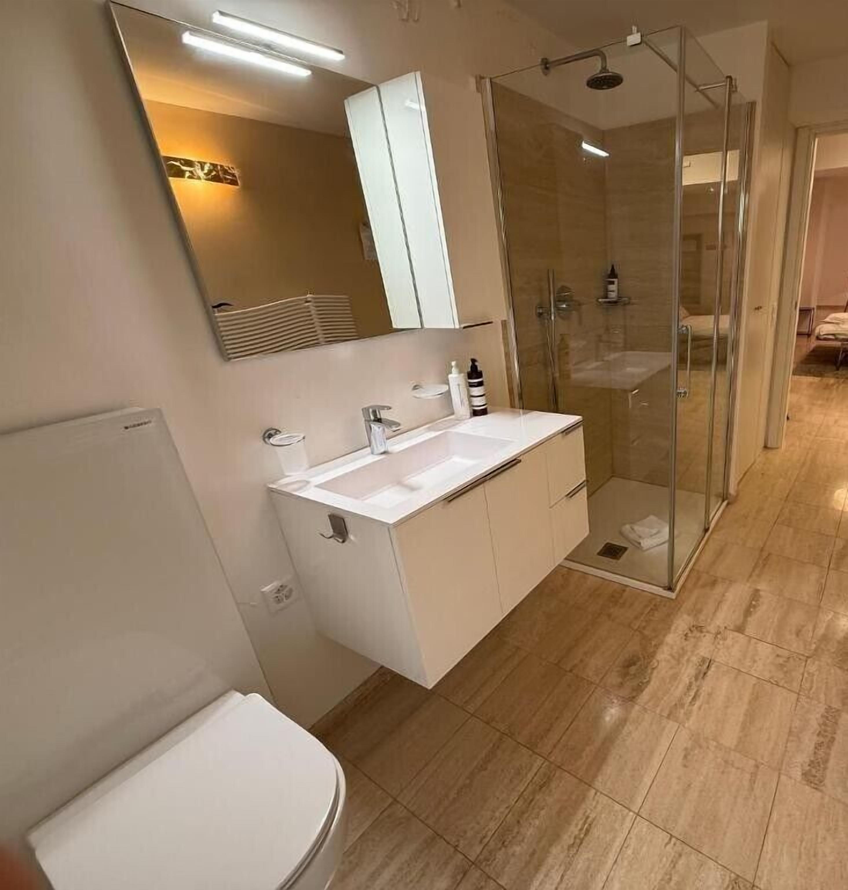 A modern bathroom with a glass-enclosed shower, a white sink, and a large mirror.
