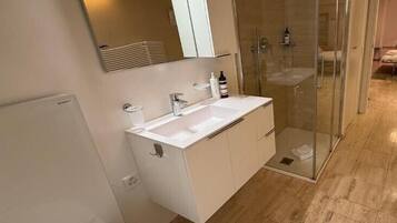 A modern bathroom with a glass-enclosed shower, a white sink, and a large mirror.