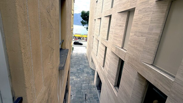 A narrow alleyway between buildings with a view of a body of water and mountains in the distance. - San Carlo Apartments (Lugano)