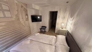 A hotel room with a large bed, a flat-screen TV mounted on the wall, a small table with a lamp, and a chair. - San Carlo Apartments (Lugano)