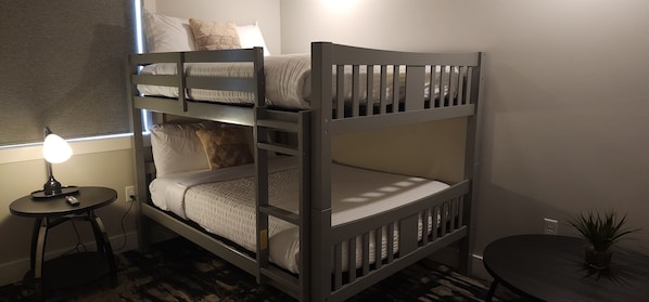 Una cama litera con escalera, una mesita de noche con lámpara y una pequeña planta en maceta.