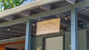 En träskylt med texten ”FLAG SPRINGS HOUSE” och ”Livet är bättre på verandan” hänger under en träkonstruktion med upphängda lampor.