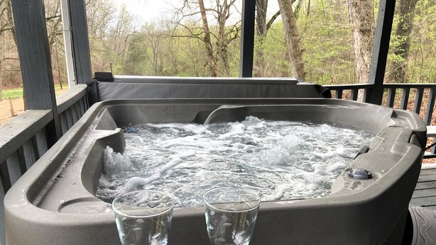 Ett bubbelbad med två glas vatten på ett bord i ett takförsett utomhusområde.