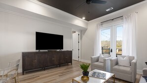 A modern living room with a flat-screen TV, wooden cabinets, a grey sofa, and a coffee table with a plant and decorative items. - 3 Bedroom, Main Level (Helena)