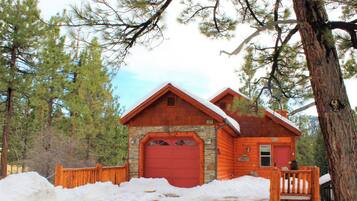 A log cabin with a stone foundation, a red garage door, and a wooden porch.