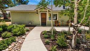 A single-story house with a front porch, a small garden with various plants, and a pathway leading to the entrance. - Cub Run Cabin (Big Bear Lake)