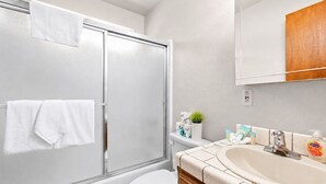 A bathroom with a glass shower enclosure, a white toilet, a vanity with a sink, and toiletries. - Cub Run Cabin (Big Bear Lake)