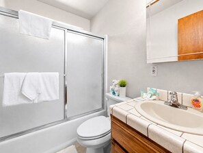 A bathroom with a glass shower enclosure, a white toilet, a vanity with a sink, and toiletries. - Cub Run Cabin (Big Bear Lake)