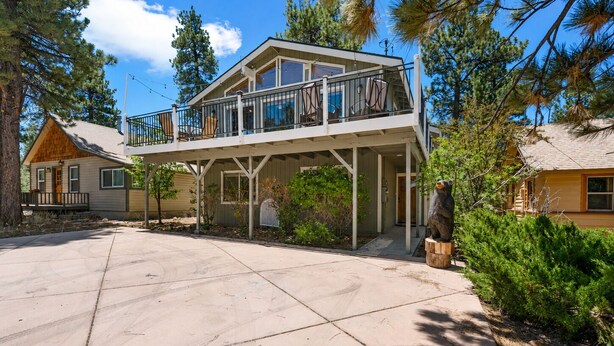 A two-story building with a balcony, a bear statue, and a clear sky. - Cub Run Cabin (Big Bear Lake)
