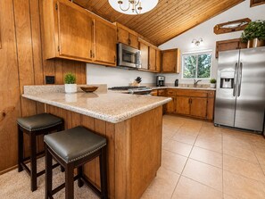 A kitchen with wooden cabinets, a stainless steel refrigerator, a granite countertop, and two bar stools. - Cub Run Cabin (Big Bear Lake)