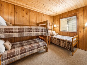 Ein Zimmer mit zwei Etagenbetten, einem Fenster mit Jalousien, einer Leiter und einer Lampe.